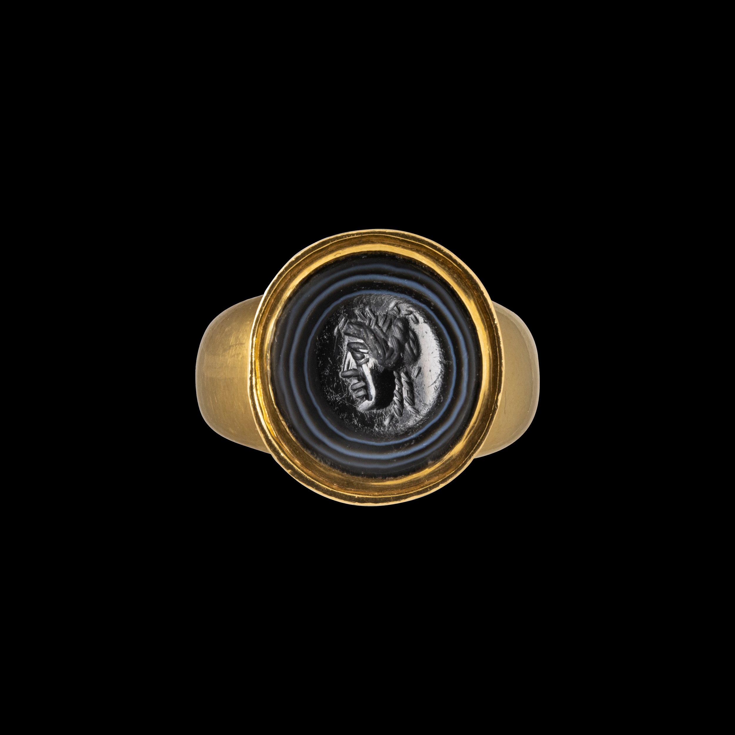 A Roman banded agate intaglio set in a gold ring. Mask. 